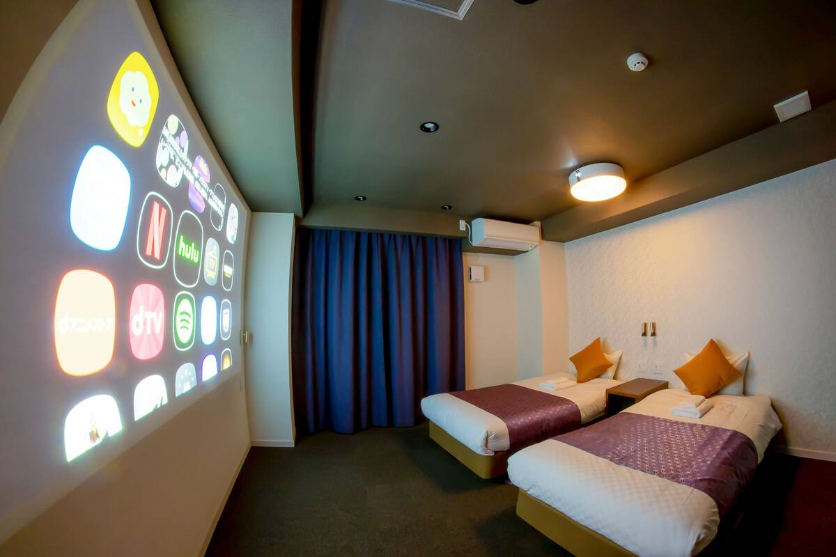 A hotel room with two beds, a ceiling light, and a wall-mounted air conditioning unit.