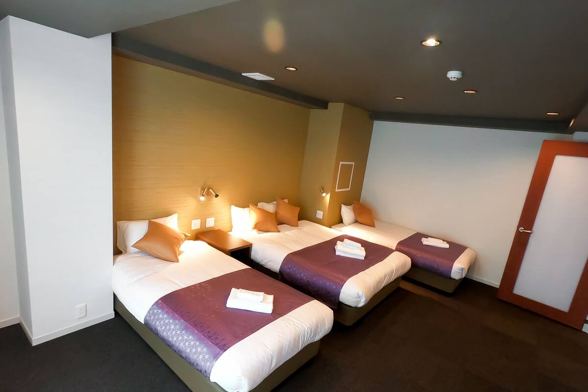 A hotel room with two beds, each with a purple and white bedspread, and a wooden headboard.