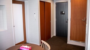 A room with a dining table, a chair, and a pink box on the table. There are three doors, one with a light switch above it.