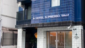 The exterior of HOTEL S-PRESSO West, featuring a modern facade with a blue and white color scheme, a visible entrance, and a security camera.