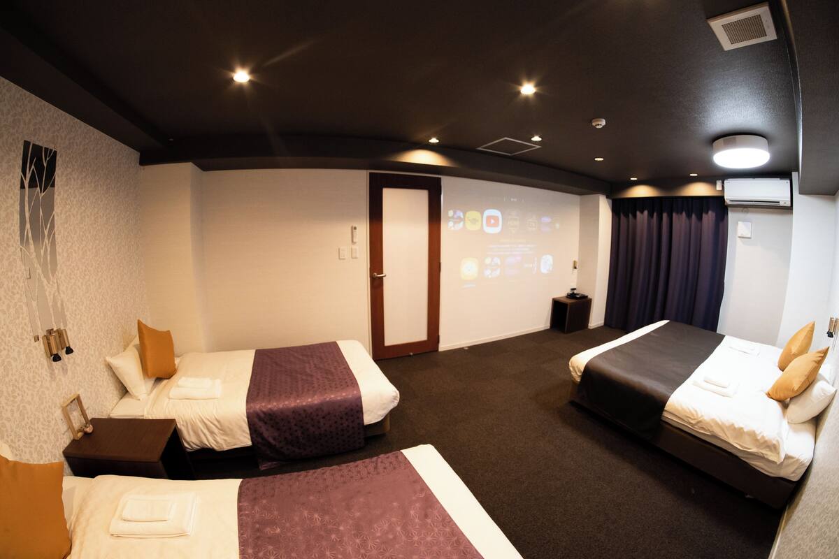A hotel room with two beds, a projector screen, a door, and a small table.