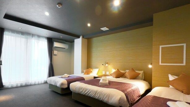 A hotel room with two beds, a large window with curtains, and a wall-mounted air conditioner.