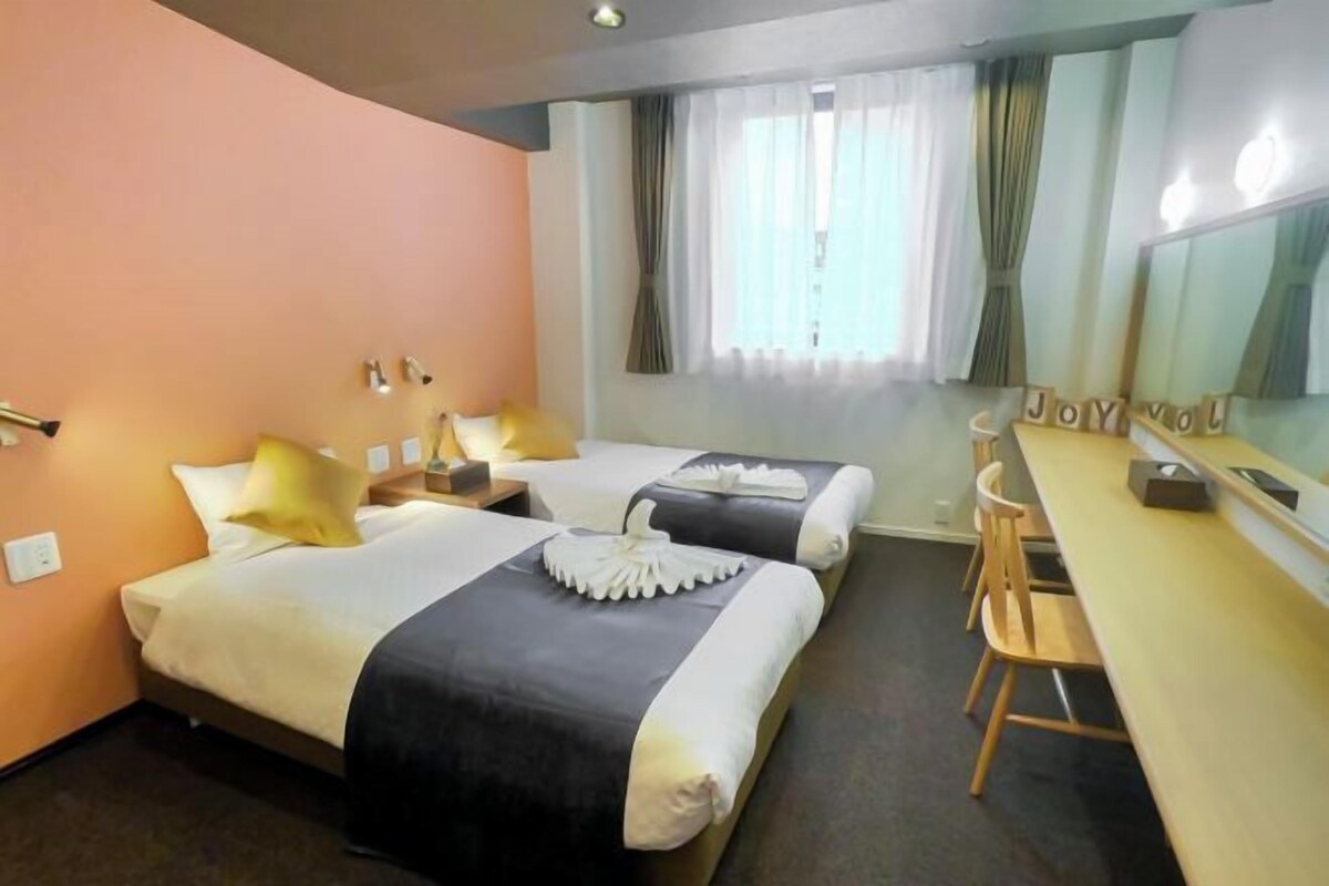 A hotel room with two beds, a desk, and a mirror.