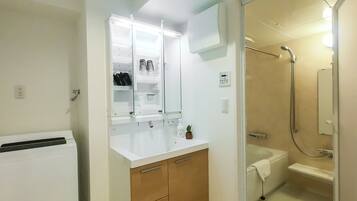 Un baño pequeño con un lavamanos blanco, armarios de madera, una cabina de ducha de vidrio y un enchufe a la vista.