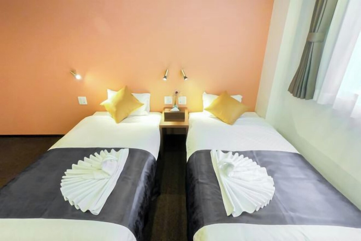 Habitación de hotel con dos camas, cada una con una almohada y una mesita de noche.
