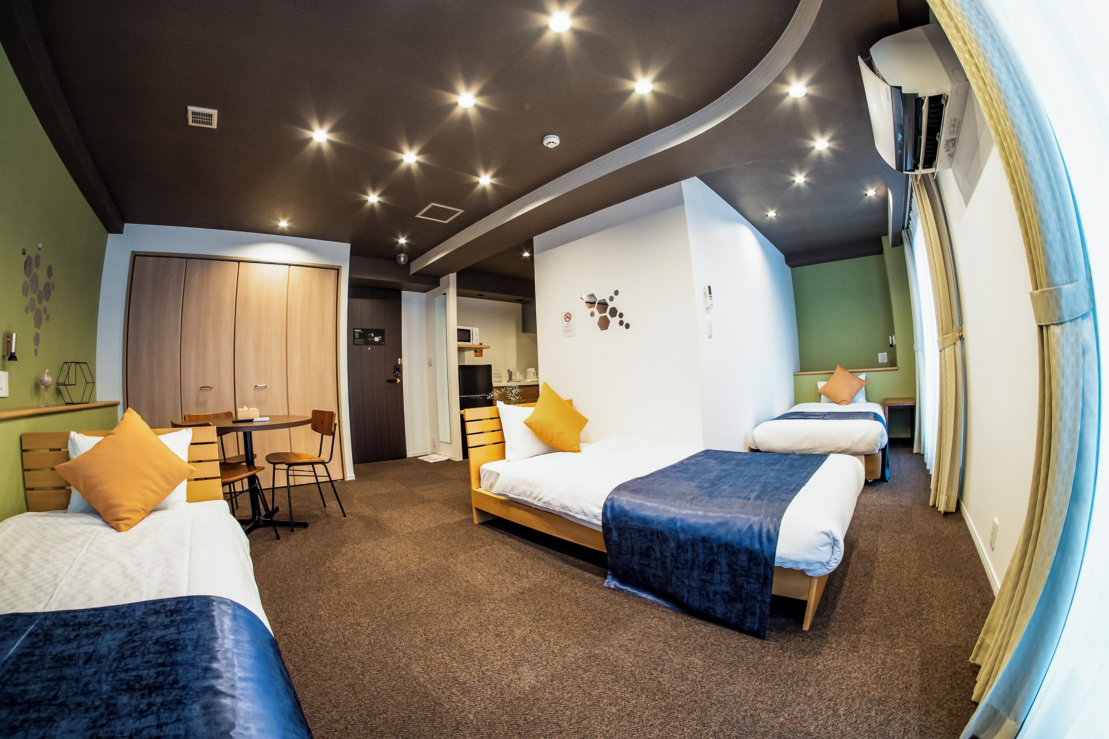 A hotel room with a bed, a desk, and a chair. There is a wardrobe and a small kitchen area.