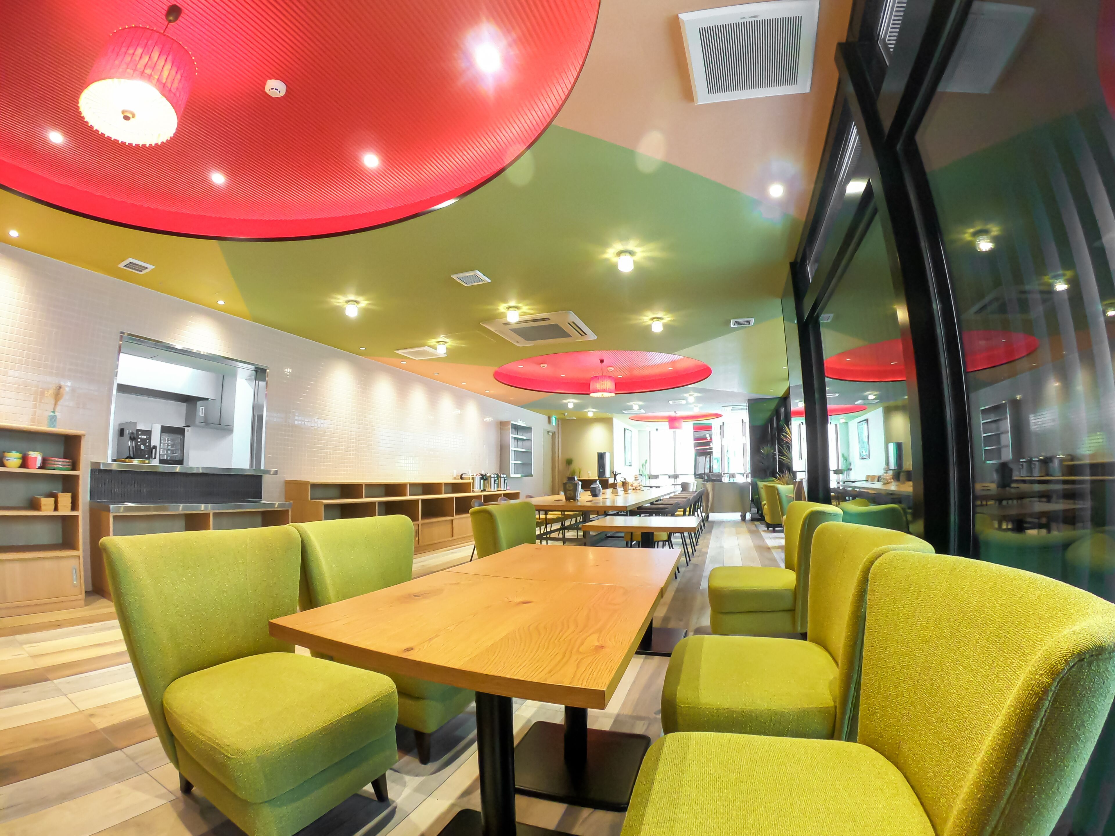 A modern restaurant interior with green upholstered chairs, wooden tables, and red ceiling lights.