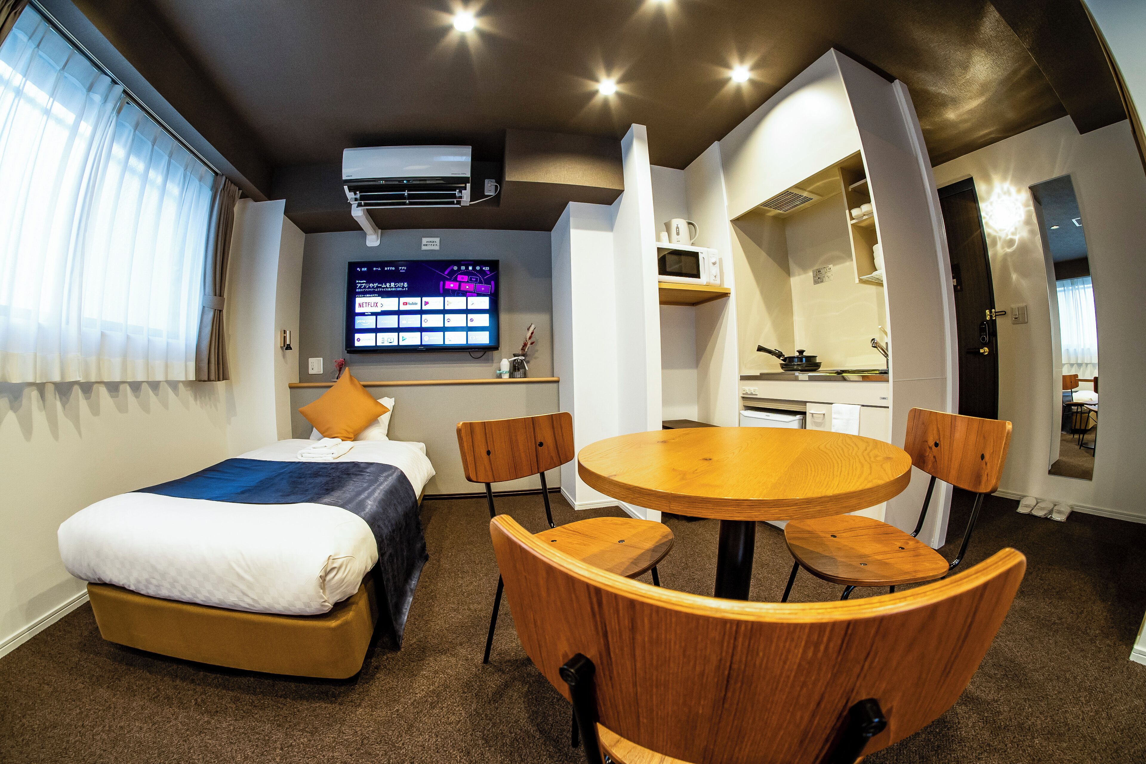 A hotel room with a bed, a desk, a TV, and a dining area with chairs.