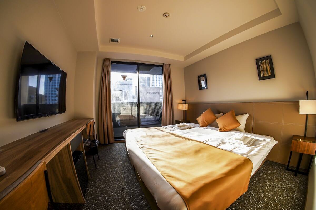 A hotel room with a bed, a desk, a TV, a window with curtains, and a city view.