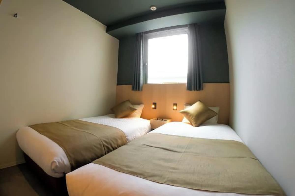 Habitación de hotel con dos camas, una ventana con cortinas y una mesita de noche.