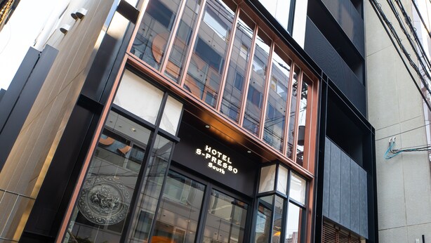 A hotel entrance with a large glass facade, a sign reading 'HOTEL S-PRESSO South,' and a metal gate at the entrance. - Hotel S-presso South (Osaka)