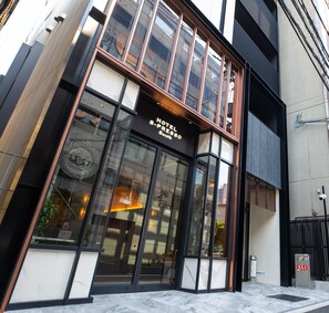 A hotel entrance with a large glass facade, a sign reading 'HOTEL S-PRESSO South,' and a metal gate at the entrance. - Hotel S-presso South (Osaka)