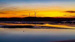 A sunset over a calm water body with wind turbines in the distance.