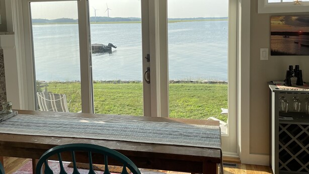A dining area with a view of a body of water, a ceiling fan, and a table with chairs.