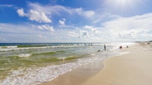 Ein Strand mit Wellen, blauem Himmel und einigen Personen.