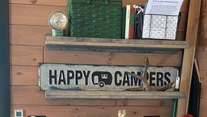 A wooden cabin interior with a 'HAPPY CAMPERS' sign, a red Daewoo microwave, and a green basket on the wall. - Moonlight Cottage “Hoot”, sleeps 5 (Rigby)