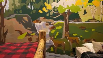 Una habitación con una cama, una colcha de cuadros rojos y negros y un mural con una escena de bosque.