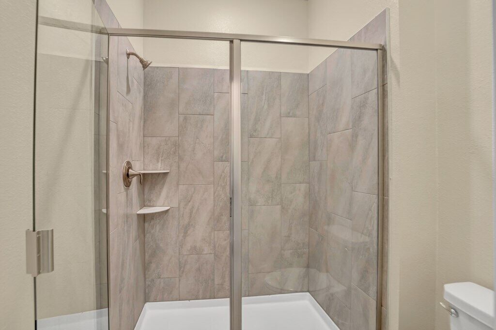A modern bathroom with a glass-enclosed shower, tiled walls, and a white toilet.