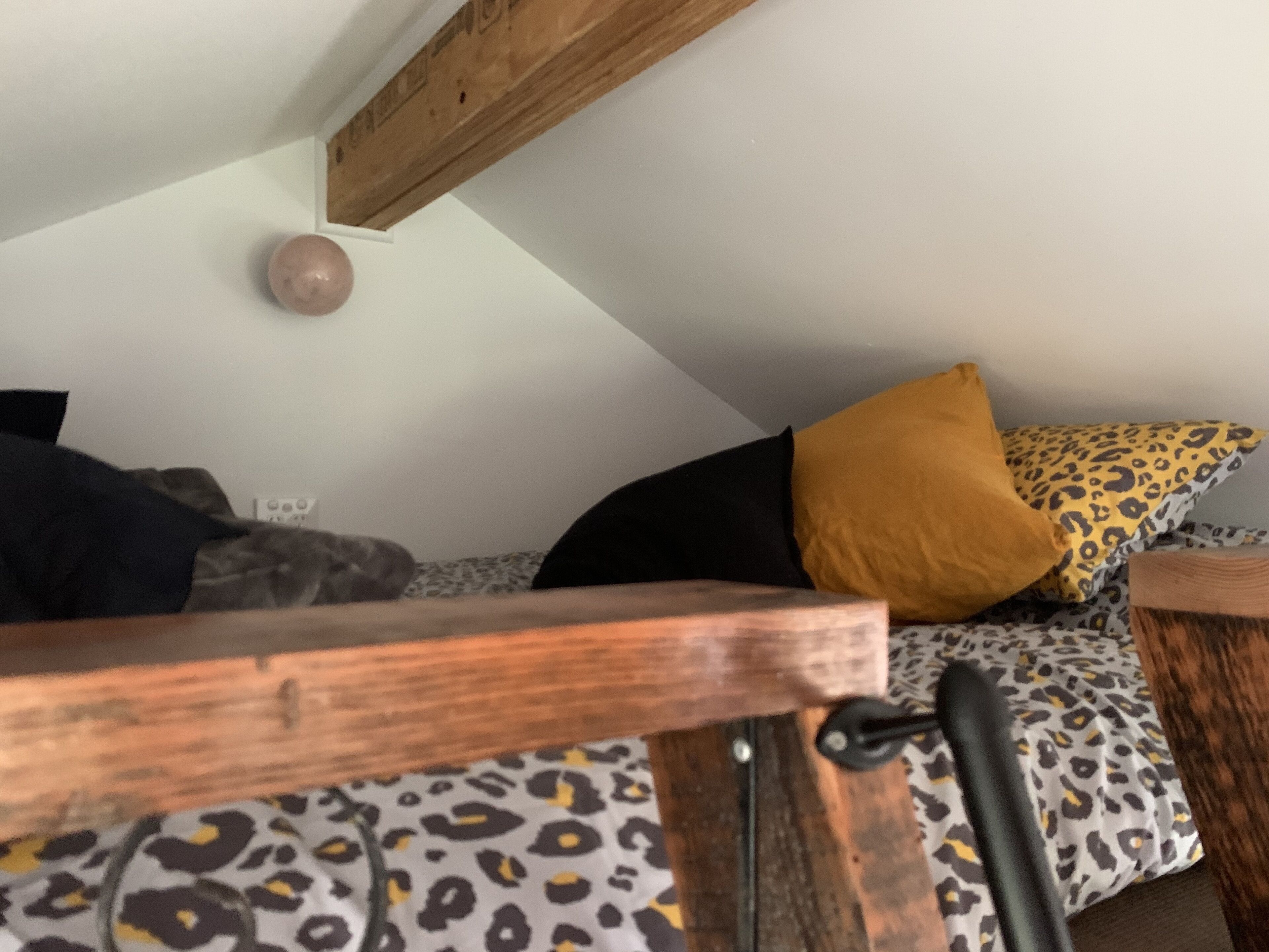 A room with a sloped ceiling, wooden beams, a bed with leopard print bedding, and a wooden headboard.
