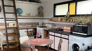 Een kleine keuken met een ronde tafel, stoelen, een wasmachine en een bed met een bedovertrek met een patroon.