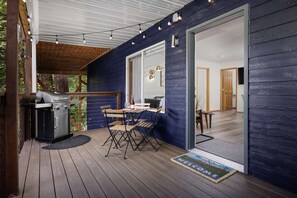 A covered outdoor area with a barbecue grill, a table with chairs, and a welcome mat.