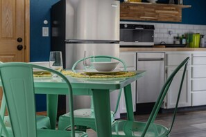 A kitchen with a stainless steel refrigerator, white cabinets, and a green table with chairs.