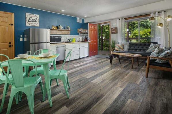 A modern kitchen with a dining area, a sofa, and a view of the outdoors.