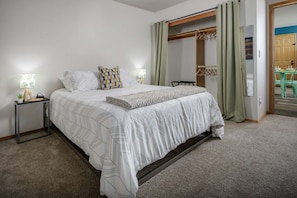 A bedroom with a bed, two bedside tables, a hanging coat rack, and a view of a dining area.