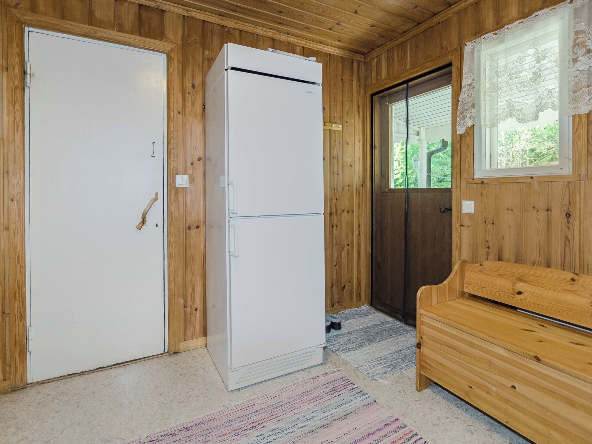 Una stanza con pareti in legno, un frigorifero bianco, una panca in legno e una porta con una finestra.