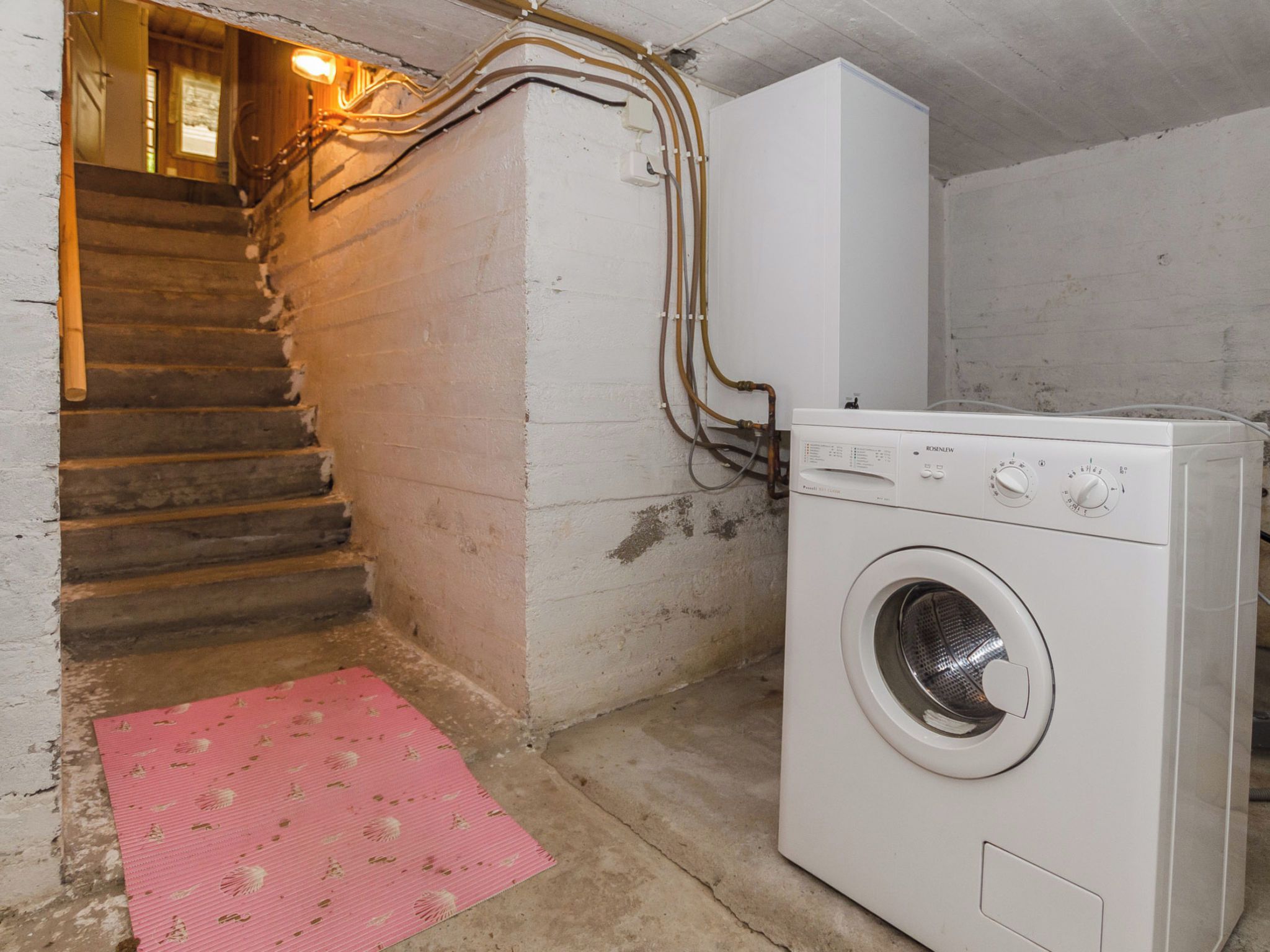 Ein Waschraum mit einer Waschmaschine, einer rosa Fußmatte und einer Treppe.
