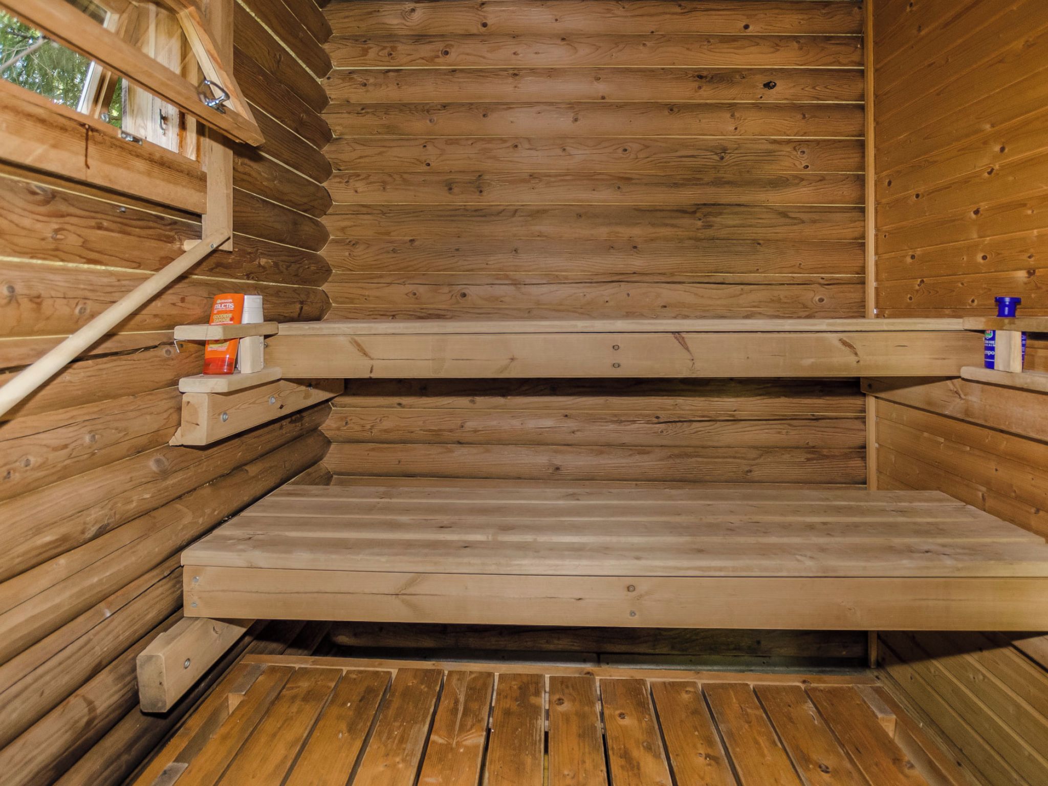 Een houten sauna met banken en een plank met flessen.