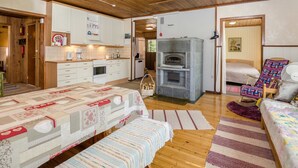 Een gezellige, goed verlichte kamer met houten vloeren, een kitchenette, een open haard en een bed met een kleurrijk sprei.
