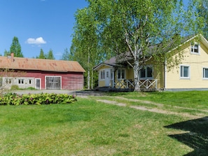 Maaseudulla sijaitseva kiinteistö, jossa on punainen lato, keltainen talo kuistilla ja suuri puu etualalla.