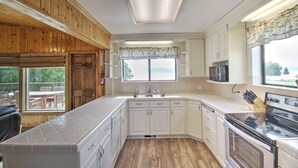 A kitchen with wooden paneling, white cabinets, a large window, and a built-in microwave.