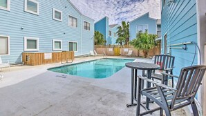 Une piscine entourée d’une terrasse en bois, elle-même bordée de bâtiments bleus aux contours blancs.