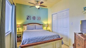 Une chambre à coucher avec un lit, un ventilateur de plafond, des lampes de chevet et un téléviseur posé sur une commode en bois.