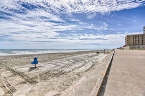 Une plage avec une promenade en béton, un panneau bleu et un bâtiment en arrière-plan.