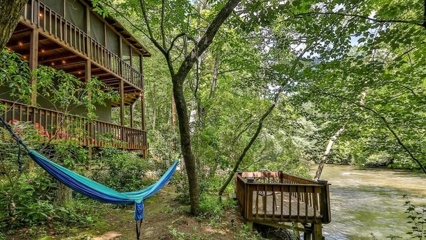 A wooden deck with a hammock and a wooden bench overlooking a river.