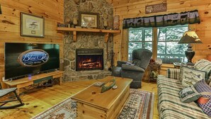 A cabin interior with a stone fireplace, a television, a sofa, and a patterned rug.