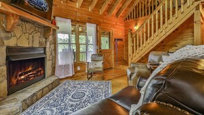A cabin with a stone fireplace, leather seating, a wooden staircase, and a sign for Blue Sky Cabin Rentals. - The Mason Jar At Cherry Log | Cherry Log, GA (Cherry Log)
