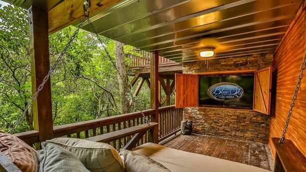 A wooden deck with a sofa and cushions, a stone wall, and a sign for Blue Sky Cabin Rentals. - The Mason Jar At Cherry Log | Cherry Log, GA (Cherry Log)