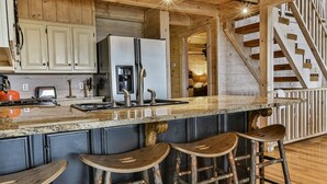 A kitchen with wooden cabinets, a granite countertop, a refrigerator, a sink, and bar stools.