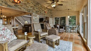 A cozy interior with a brick wall, wooden ceiling, and a fireplace. There are leather chairs, a sofa, and a dining table with chairs.