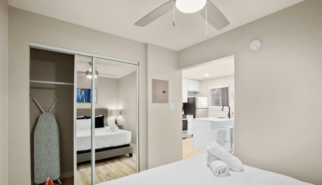 Een moderne hotelkamer met een bed, een garderobe, een plafondventilator en uitzicht op de keukenhoek.