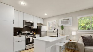 A modern kitchen with white cabinetry, stainless steel appliances, and a central island with bar stools.