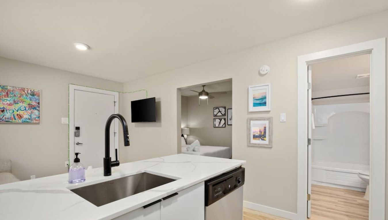 Een moderne keuken met een groot eiland, een ingebouwde vaatwasser en een spoelbak. Er is een televisie aan de muur bevestigd en kunstwerken erboven.