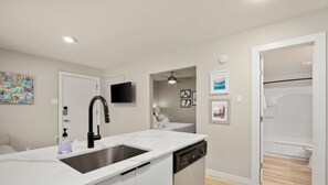 A modern kitchen with a large island, built-in dishwasher, and a sink. There is a television mounted on the wall and artwork displayed above it.