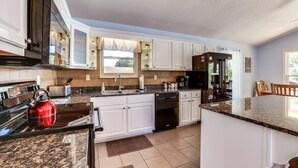 A modern kitchen with white cabinets, granite countertops, a red kettle, and a dishwasher. - Watts Bar Lake Escape: Private Boat Dock + Ramp! (Spring City)