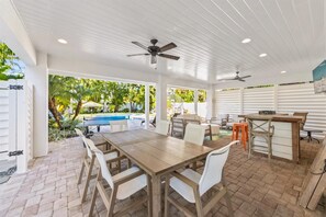 Un patio al aire libre con mesa y sillas de madera, una piscina y un ventilador de techo.