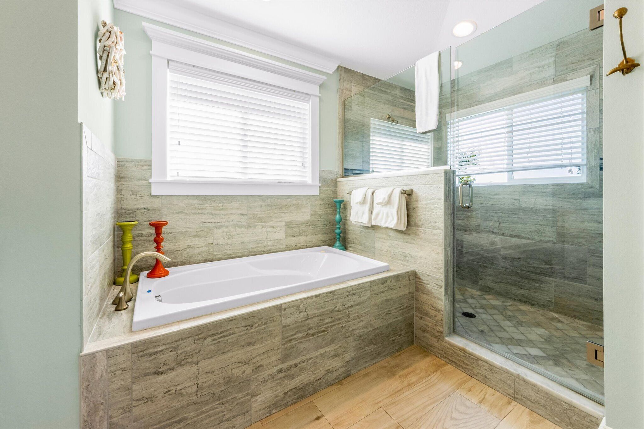 Un baño moderno con una bañera independiente, ducha con mampara de vidrio y ventana con persianas.